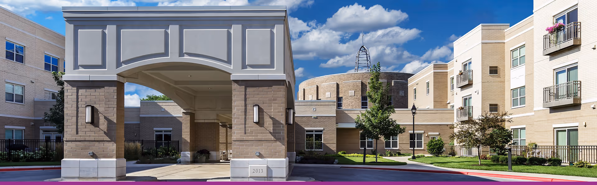 Exterior view of Mercy Circle Senior Living with a covered entrance, brick pillars, and landscaped grounds.