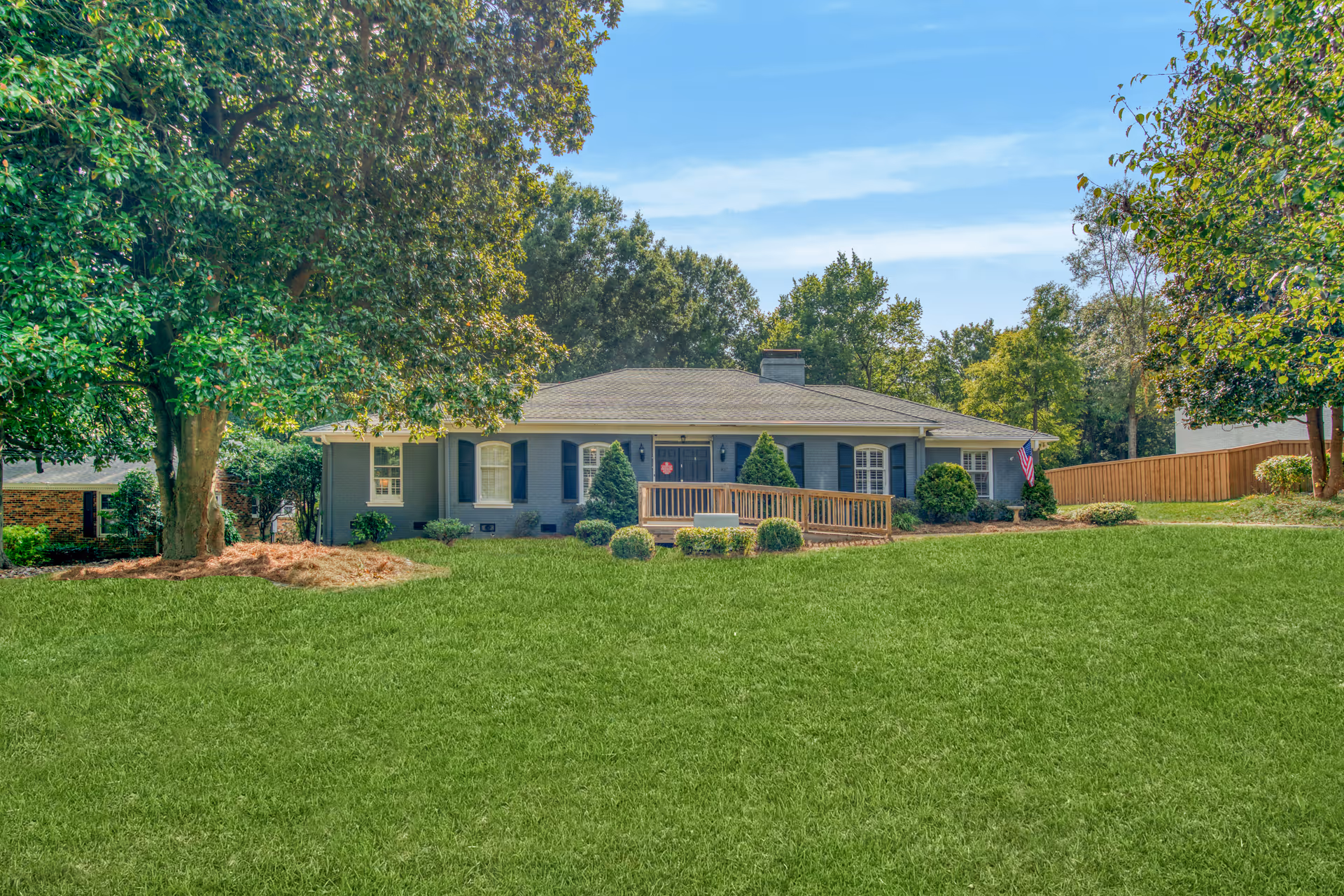 Single-story blue-gray senior living facility with a front porch, lush lawn, and mature trees.