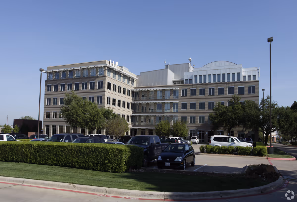 Exterior view of a large modern building with a surrounding parking lot and trees.
