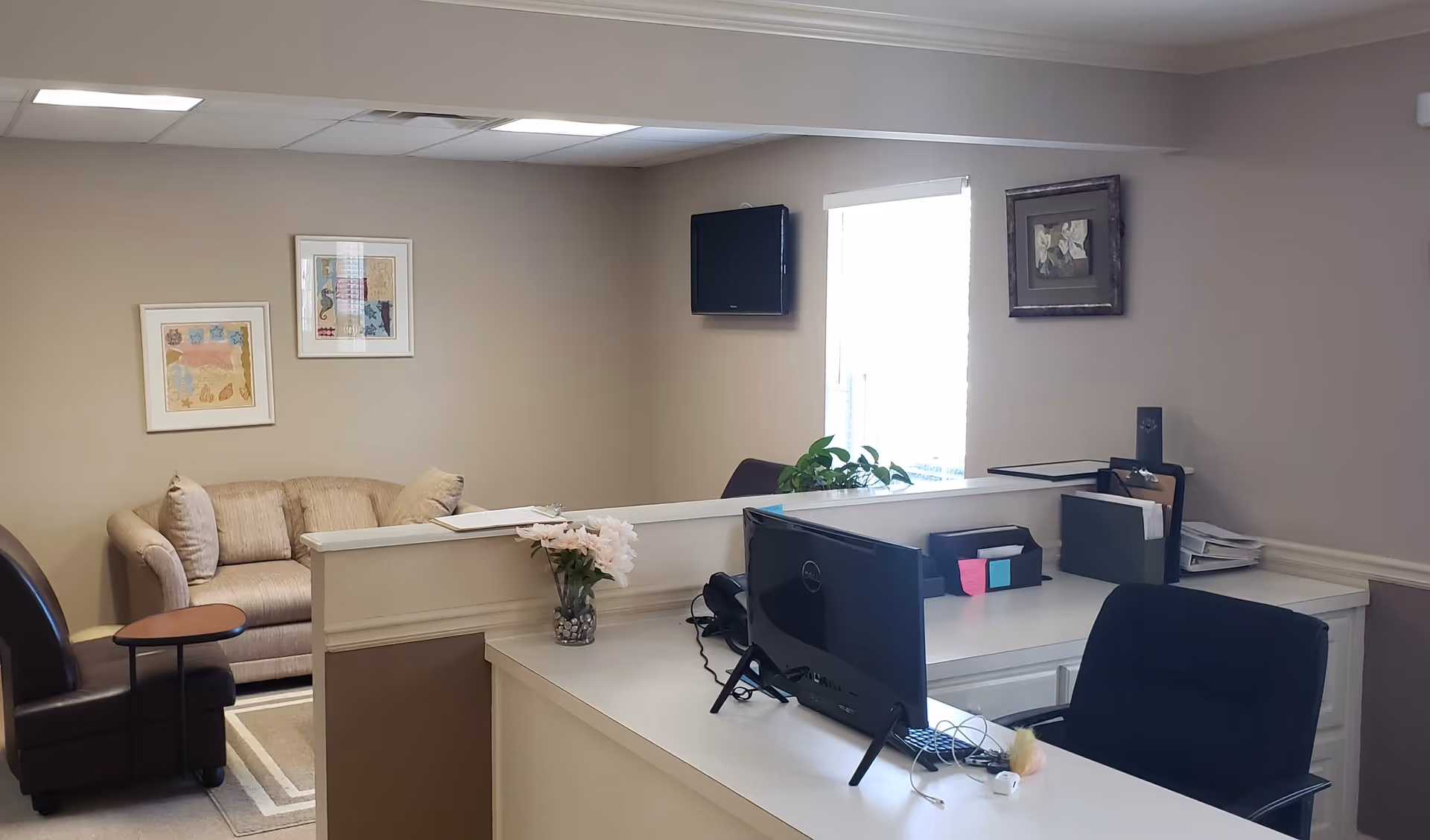 Reception desk with computer, seating area, and framed art in a quiet lobby.