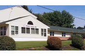 Front exterior of Mosser Nursing Home with white siding and green shrubs.