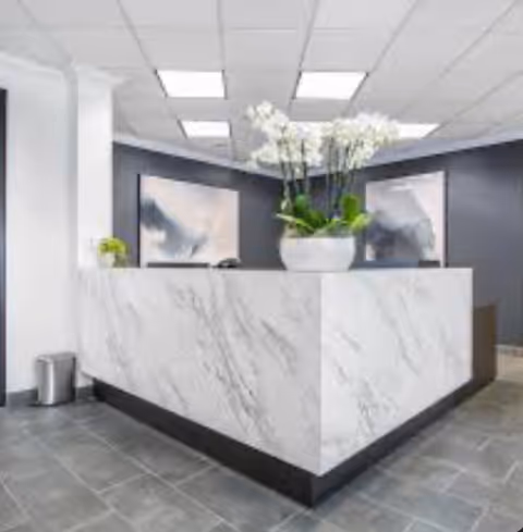 White marble reception desk in a modern lobby with plants and framed artwork.