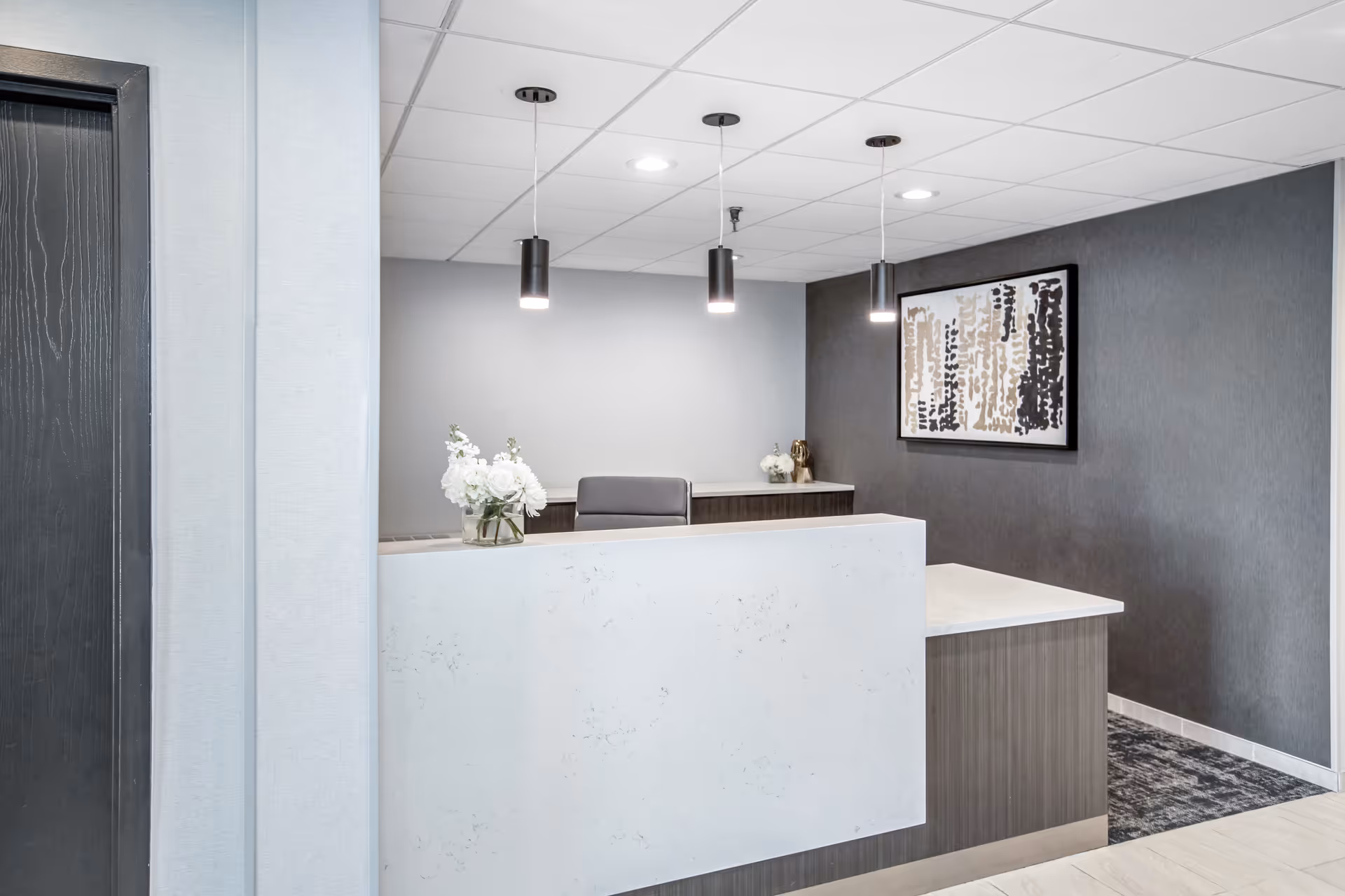 Modern reception desk in a gray-toned senior living lobby with pendant lights.