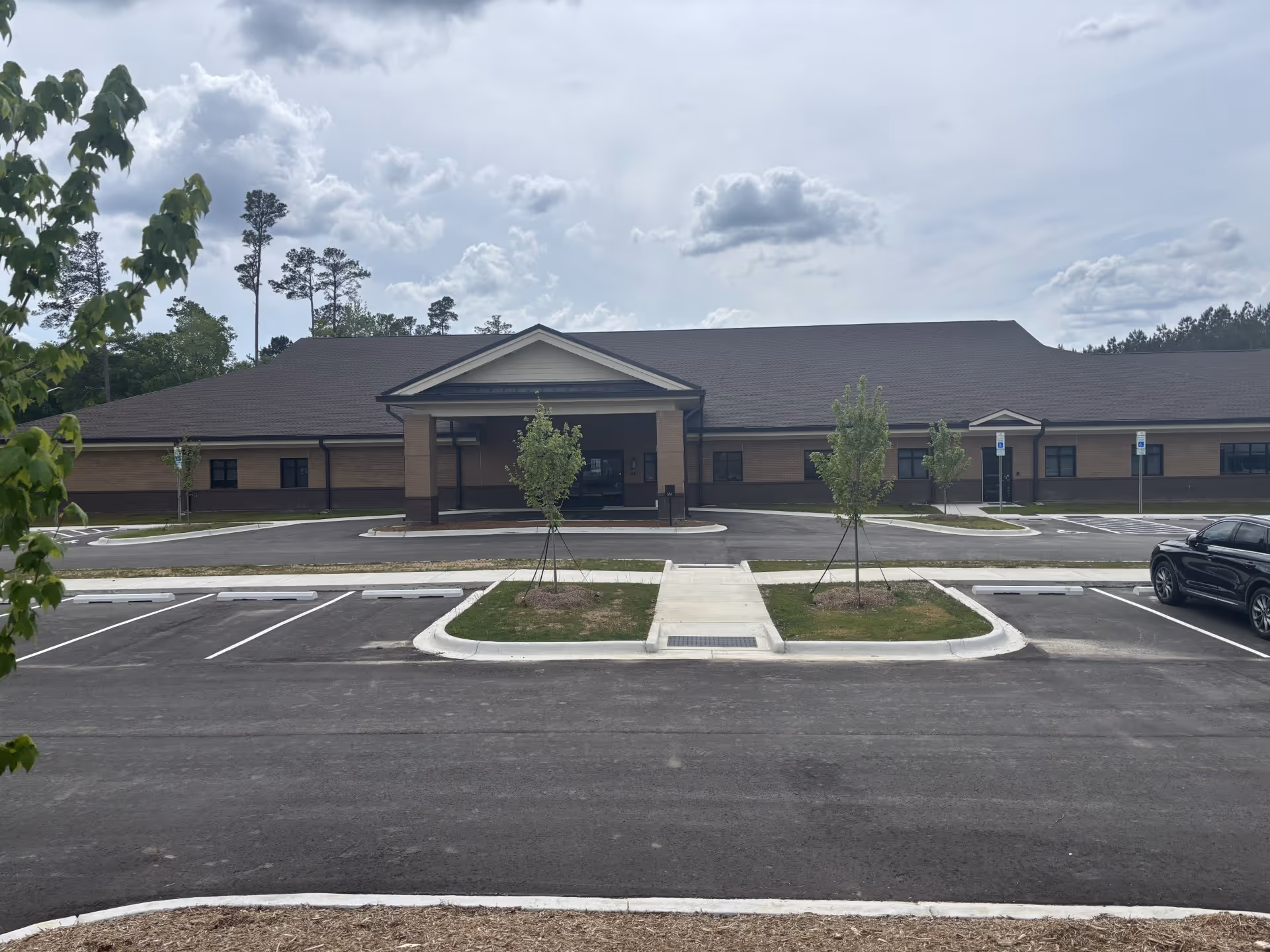 Front view of a single-story brick senior care facility with a covered entrance and parking lot.