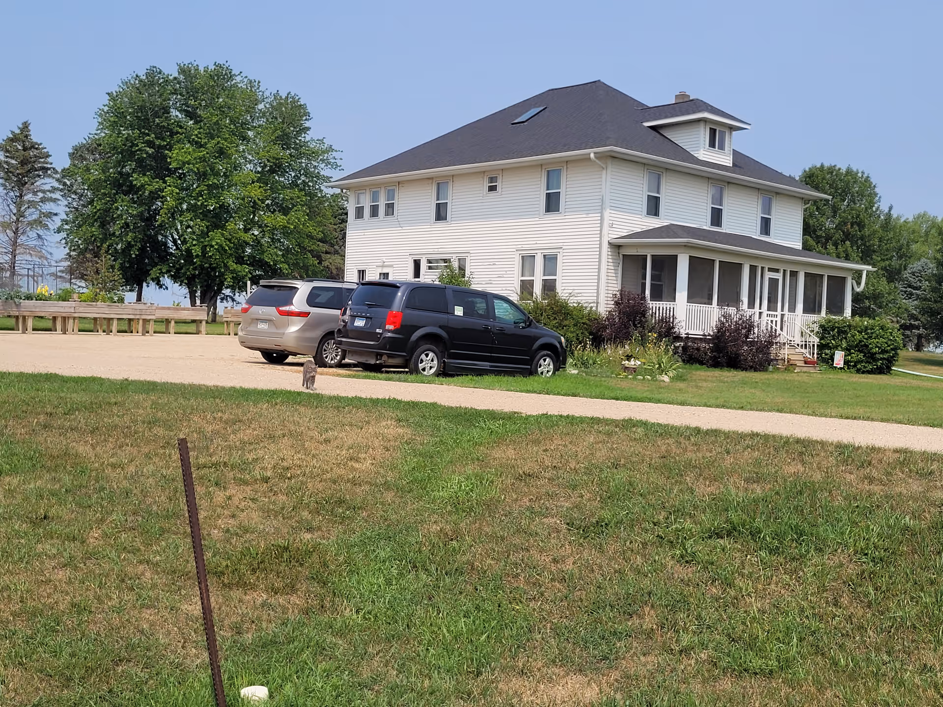 White two-story senior living facility with wraparound porch and parked cars.