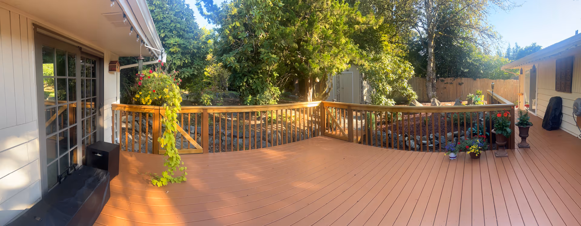 Wide wooden deck overlooking a garden with potted plants and trees surrounding the home