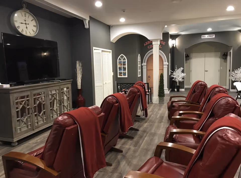 Indoor senior living lounge with red recliner chairs, a TV, and decorative arches.