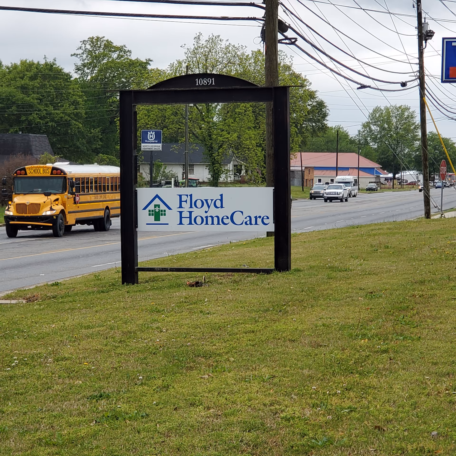 Exterior roadside view of Floyd HomeCare sign near Summerville, with a school bus and traffic.