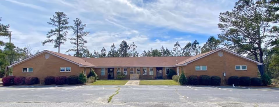Single-story brick senior living facility with a central entrance and parking.