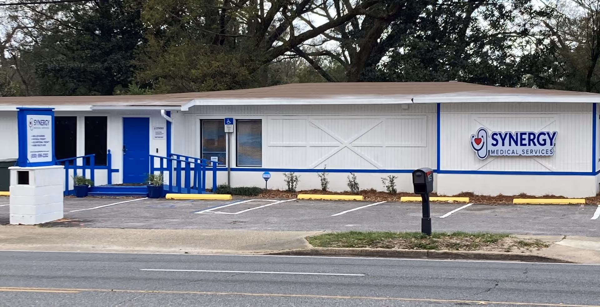 Front view of a Synergy Medical Services building with blue ramp and sign.