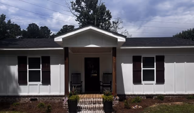 A single-story white facility with a centered front entrance, small porch, rocking chairs, and planters.