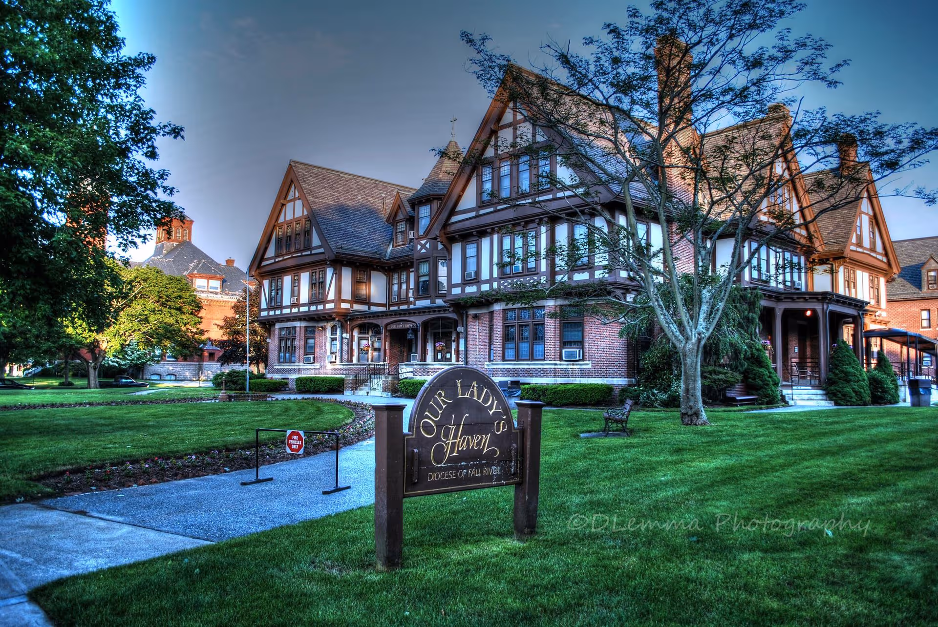 Tudor-style brick building with stone accents sits on a manicured lawn, Our Lady's Haven sign.