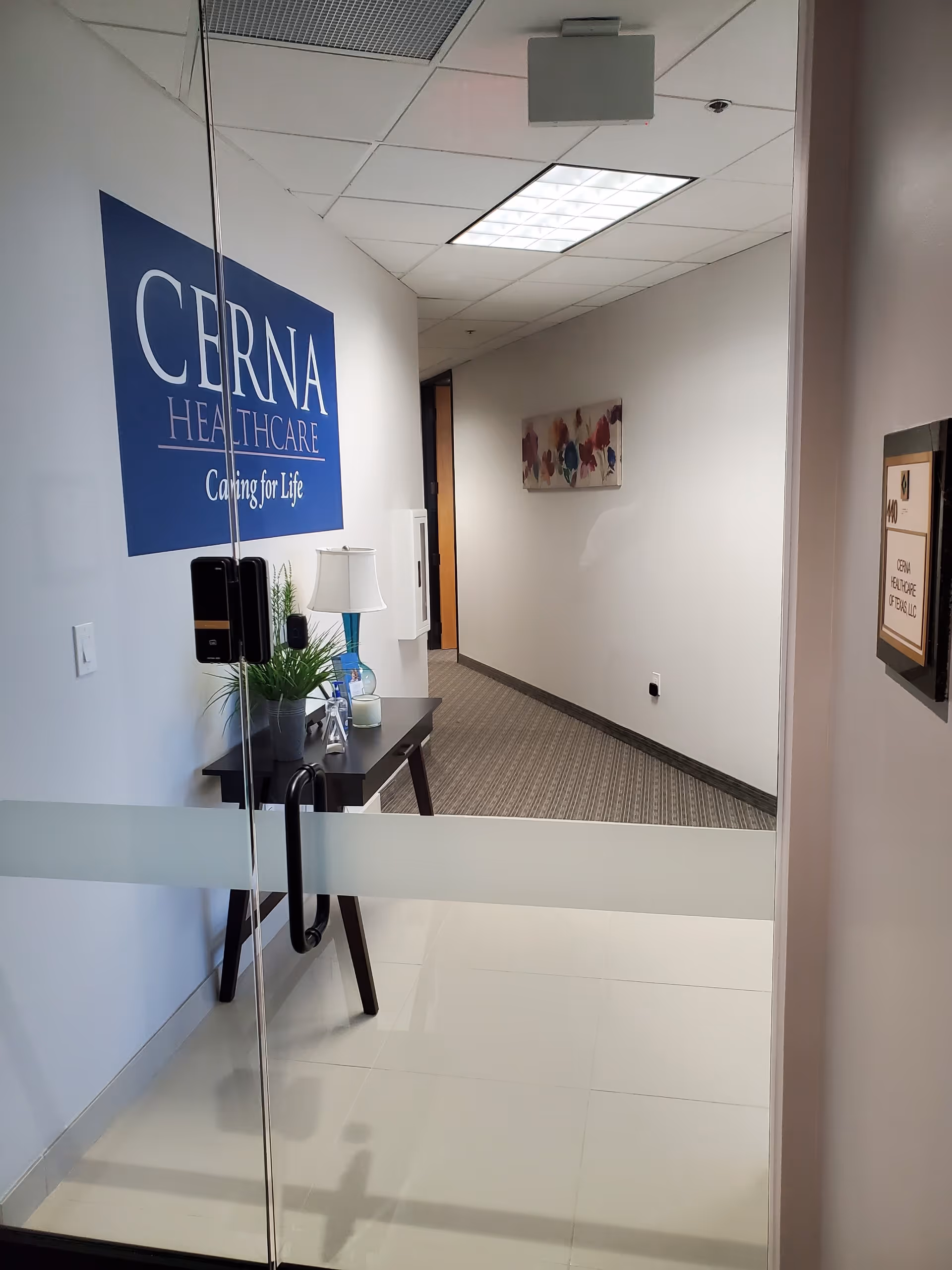 Interior corridor of Cerna Home Care with glass door and sign on wall.