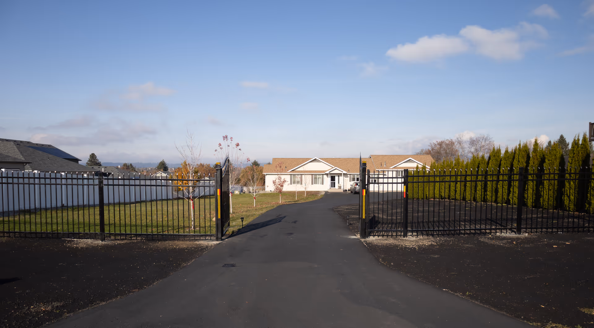 Gated driveway leads to a single-story senior living facility with a fenced yard.