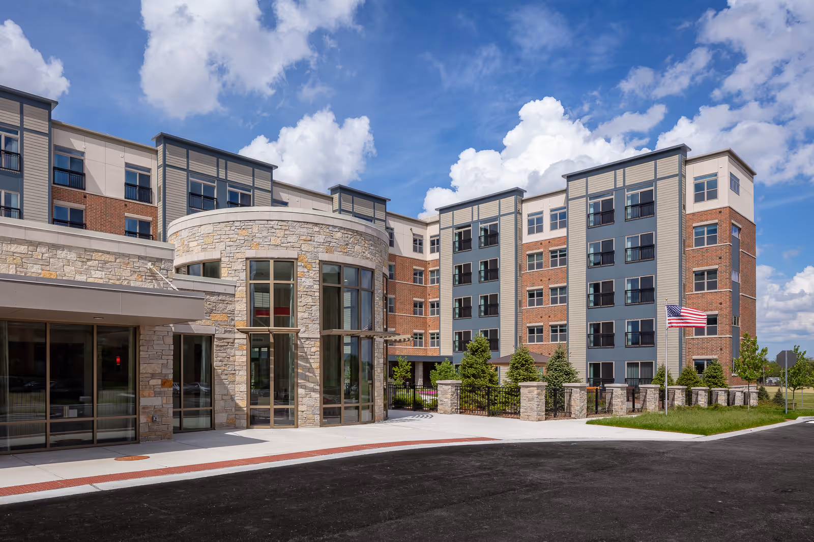 Modern senior living building with brick and stone facade, glass entry, and blue sky.