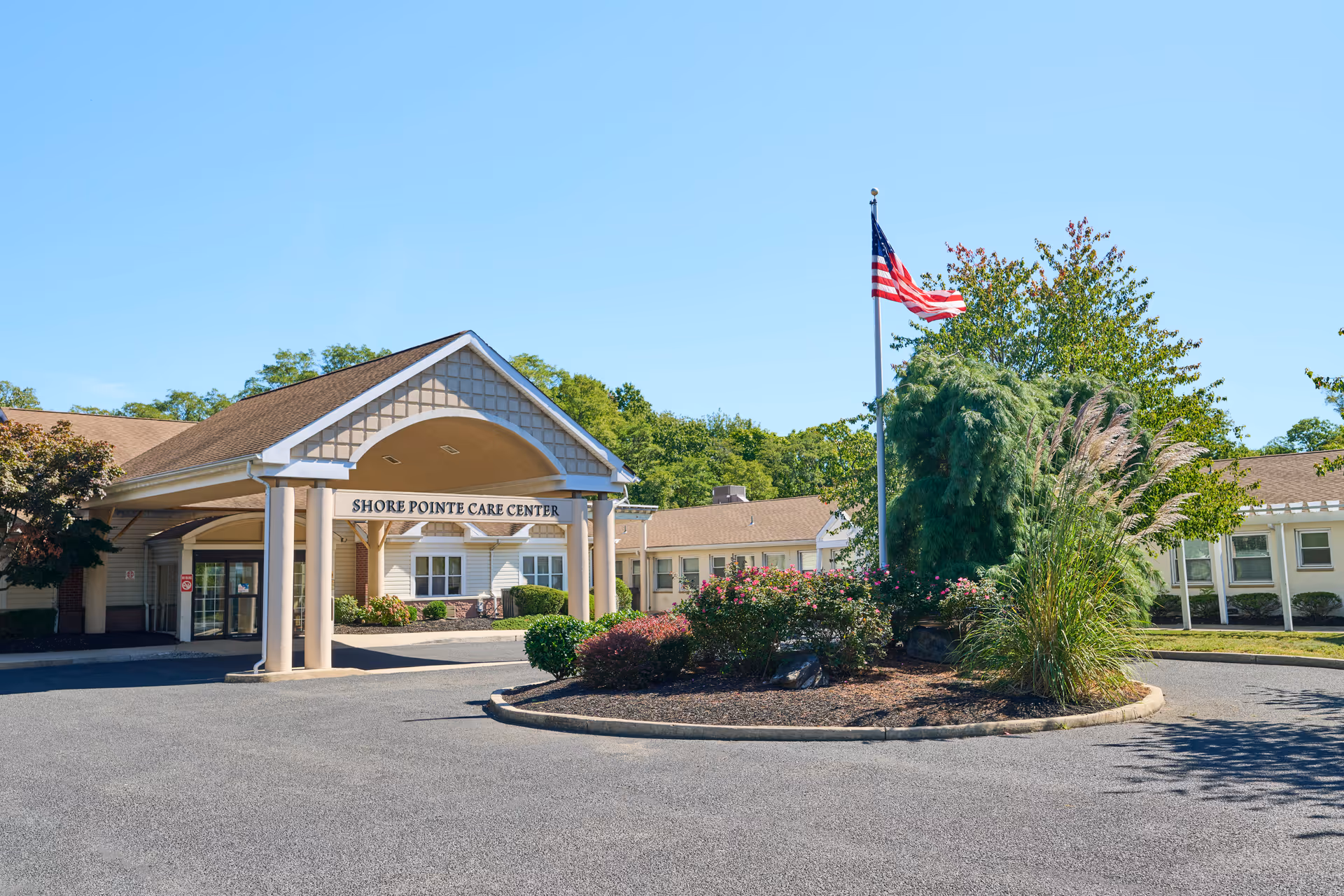 Front view of Shore Pointe Care Center with entrance arch, flagpole, and landscaped circular island.