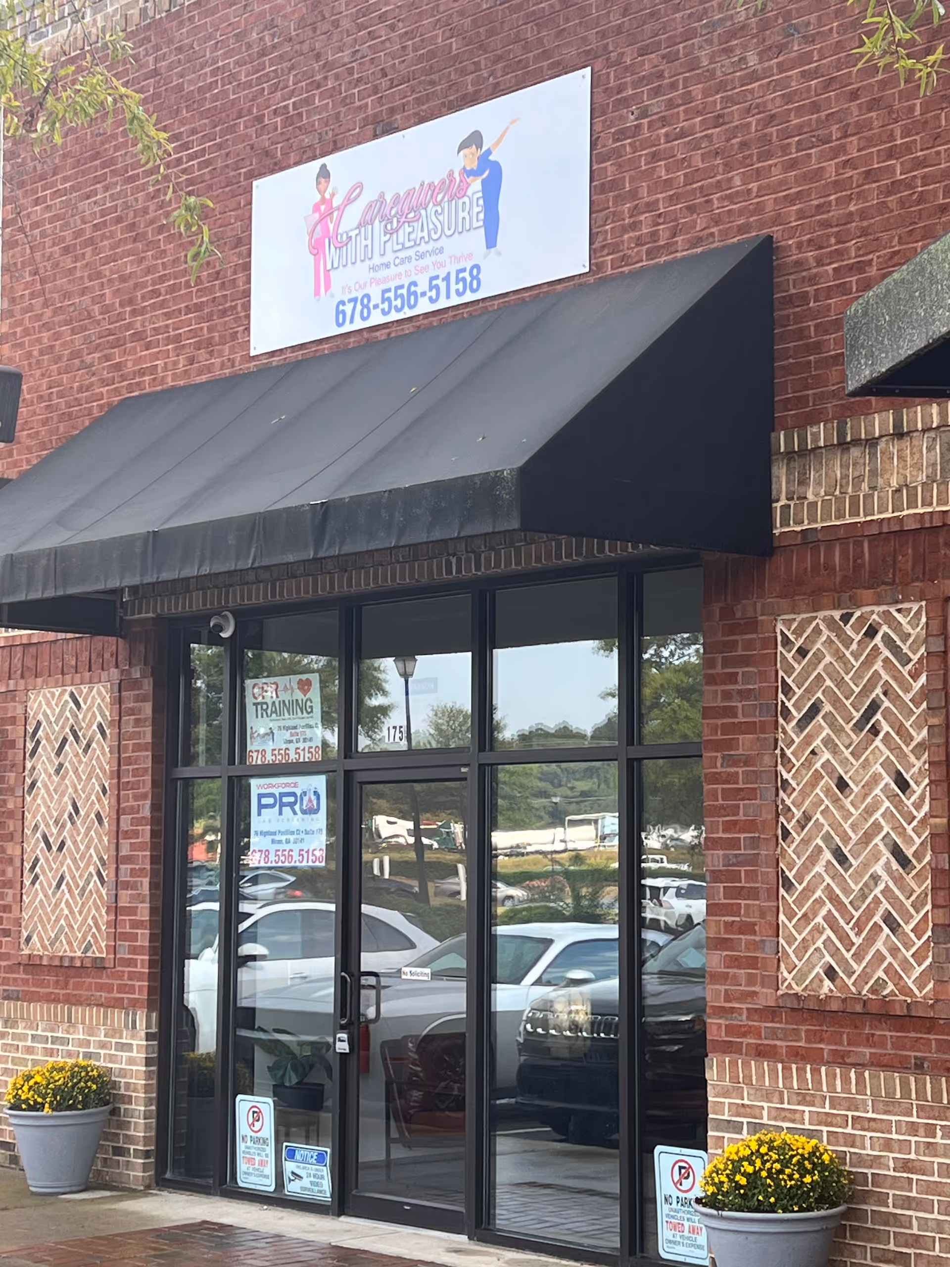 Brick storefront with black awning and glass doors; potted plants flank entrance.
