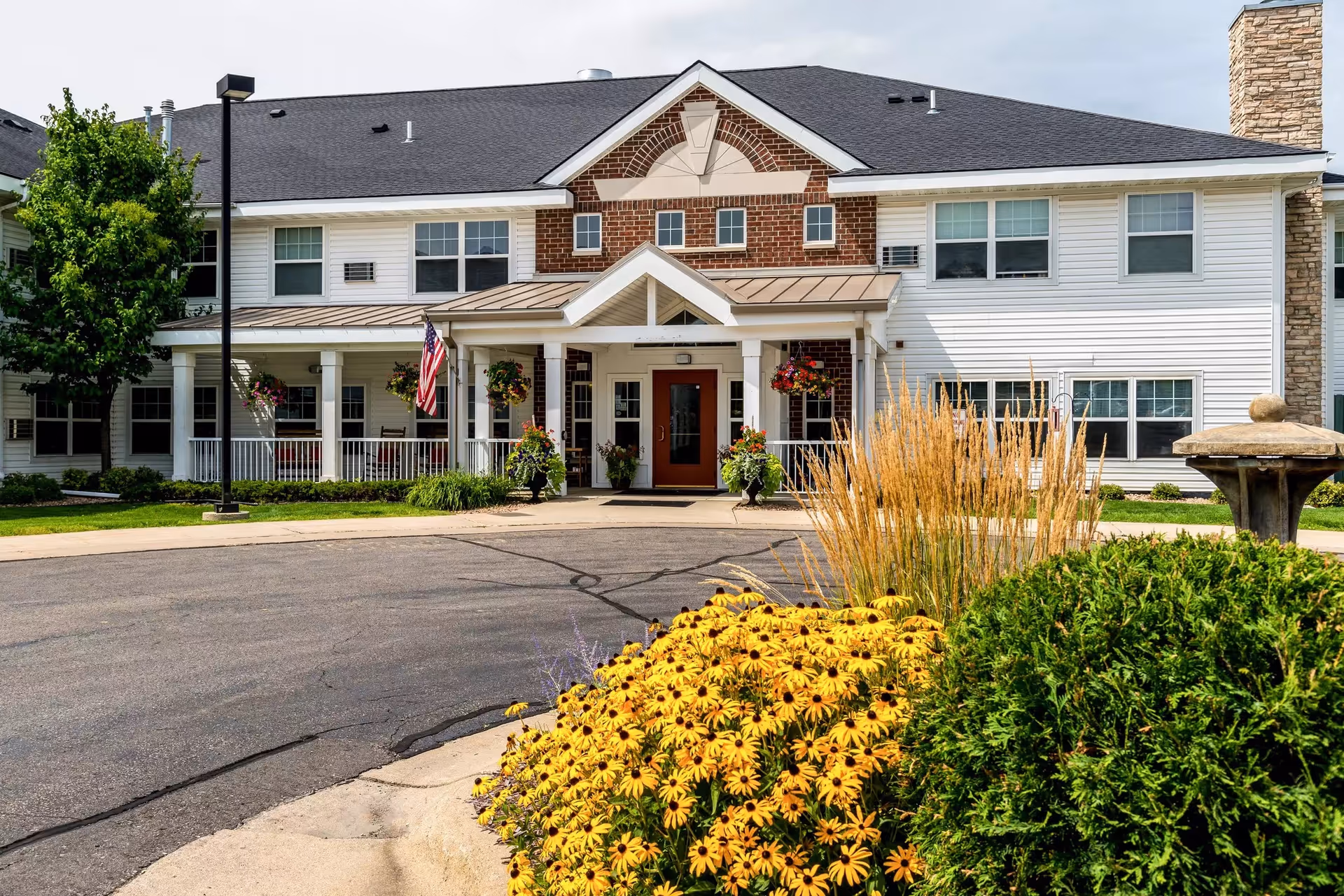 Front view of a senior living facility with entrance, landscaping, and a fountain.