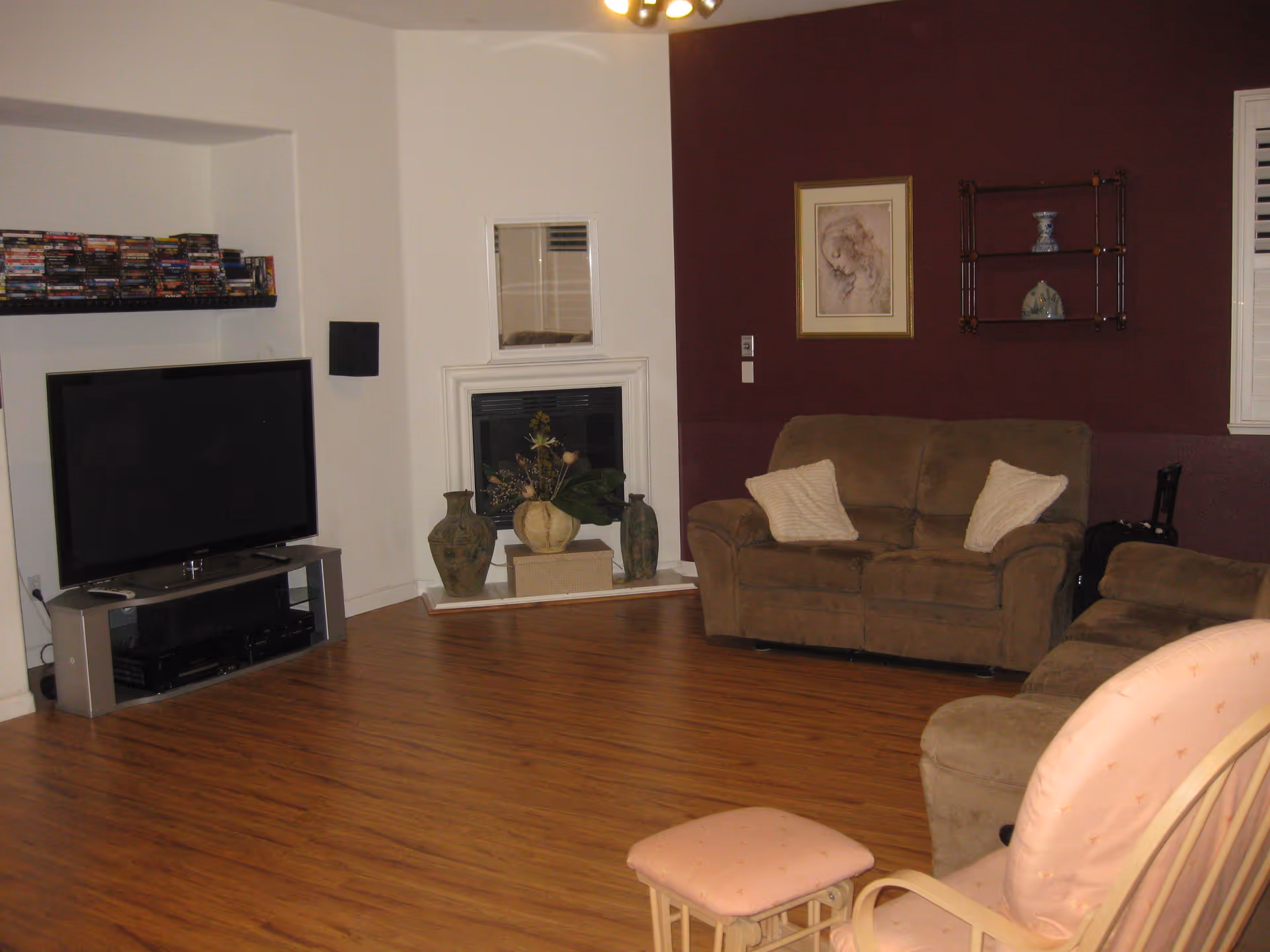 Cozy living room with hardwood floors, a TV and media console, brown sofas, a fireplace, and wall shelves.