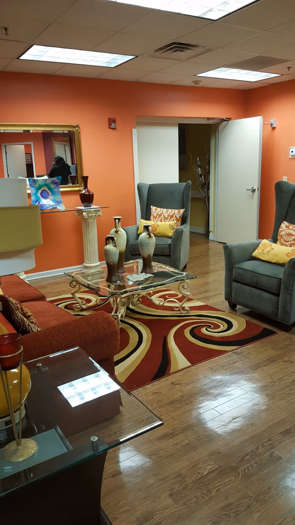 Interior lounge with orange walls, comfortable seating, glass coffee table, and swirled rug.