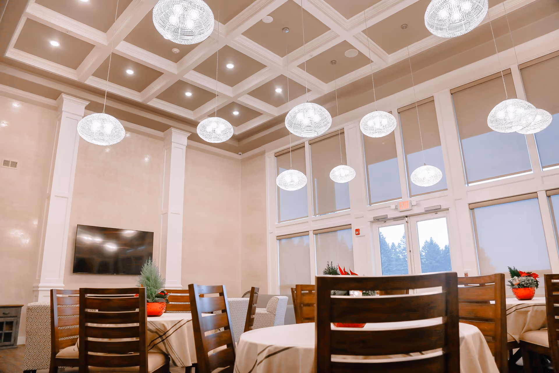 Well-lit dining room with round tables, wooden chairs, and hanging crystal lights.