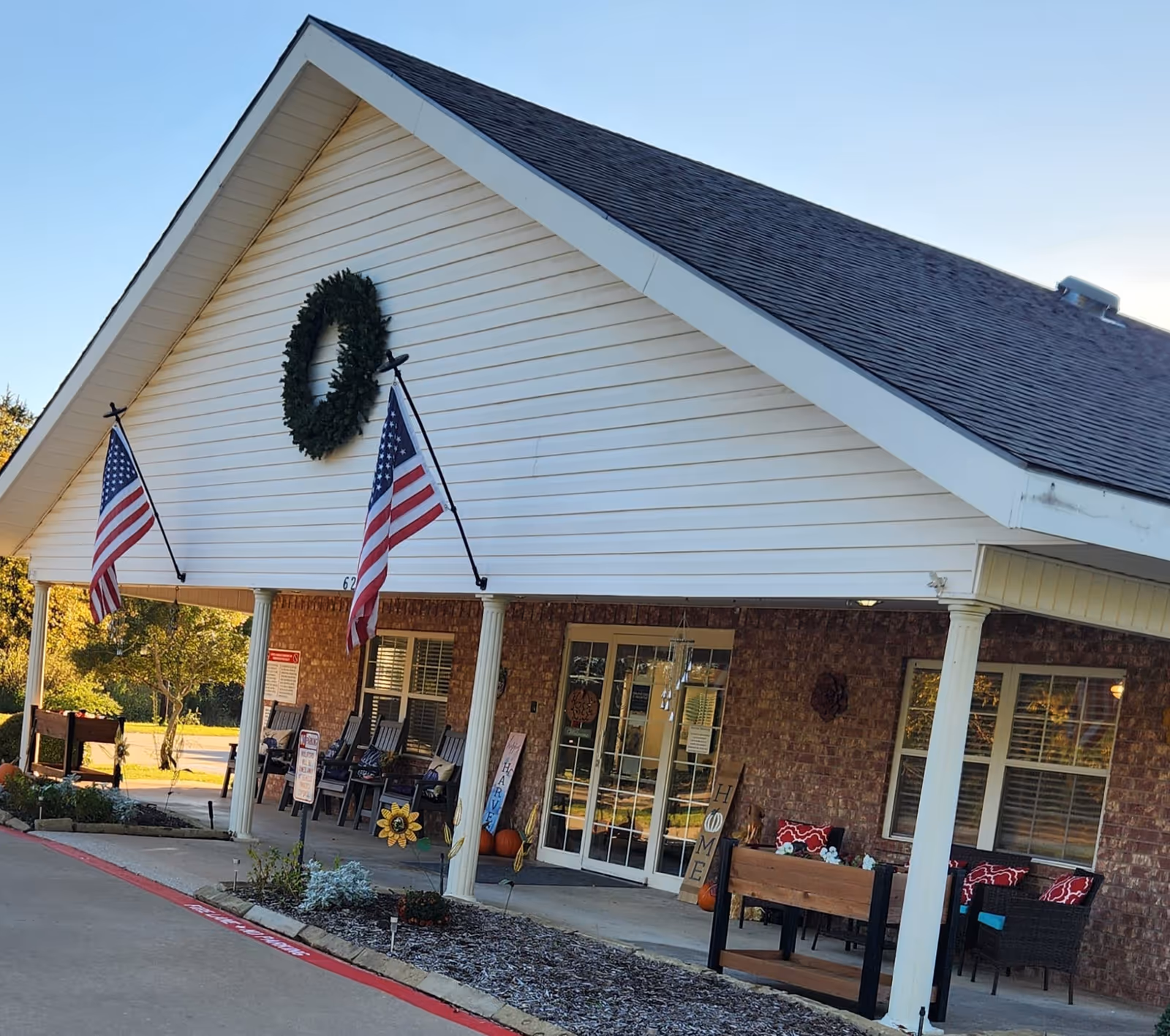 Front entrance of Preston Place senior living with American flags, wreath, and seating.