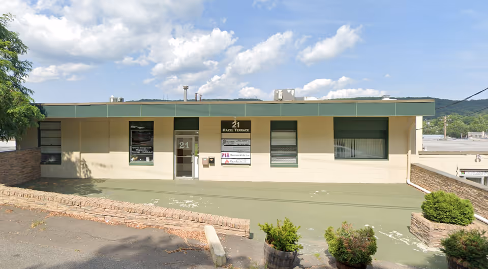 Front view of a single-story beige building with a green awning, signs, and an entrance.