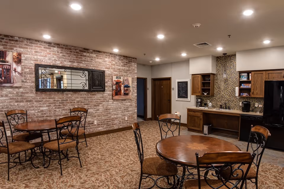Common dining area with brick accent wall, round tables, chairs, and a small kitchenette.