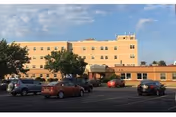 Beige, multi-story nursing home building with a parking lot in front.