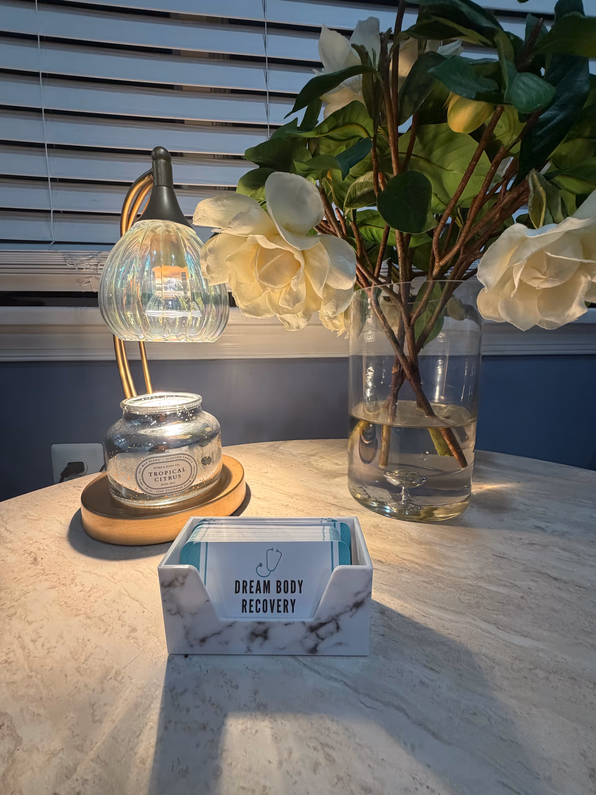 Close-up of a marble countertop with a vase of white flowers and a small lamp.