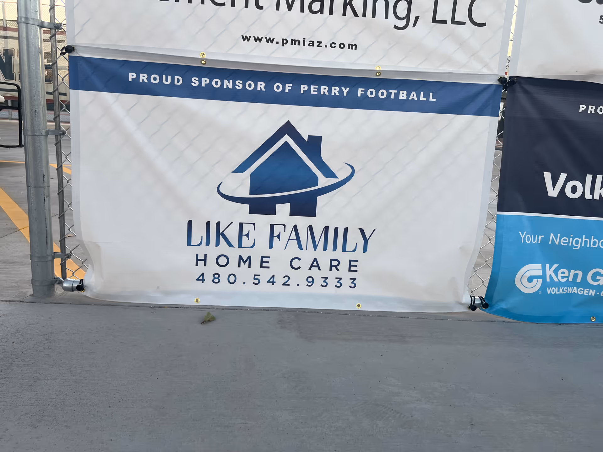 Outdoor fence banners advertising Like Family Home Care with logo and contact info.