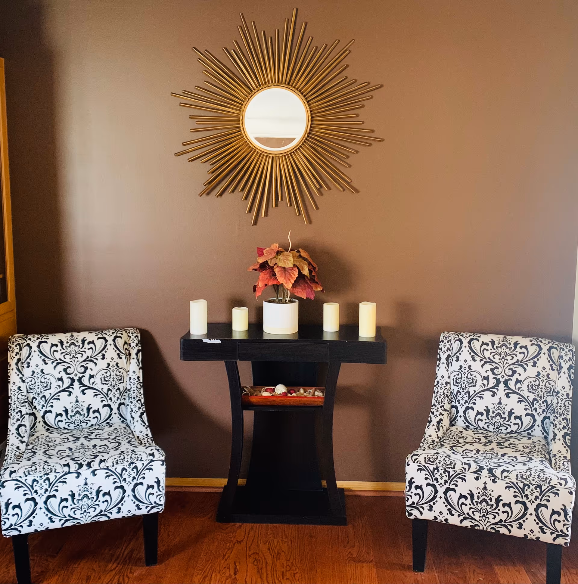 Symmetrical seating area with patterned chairs, a dark console table, and a sunburst mirror.