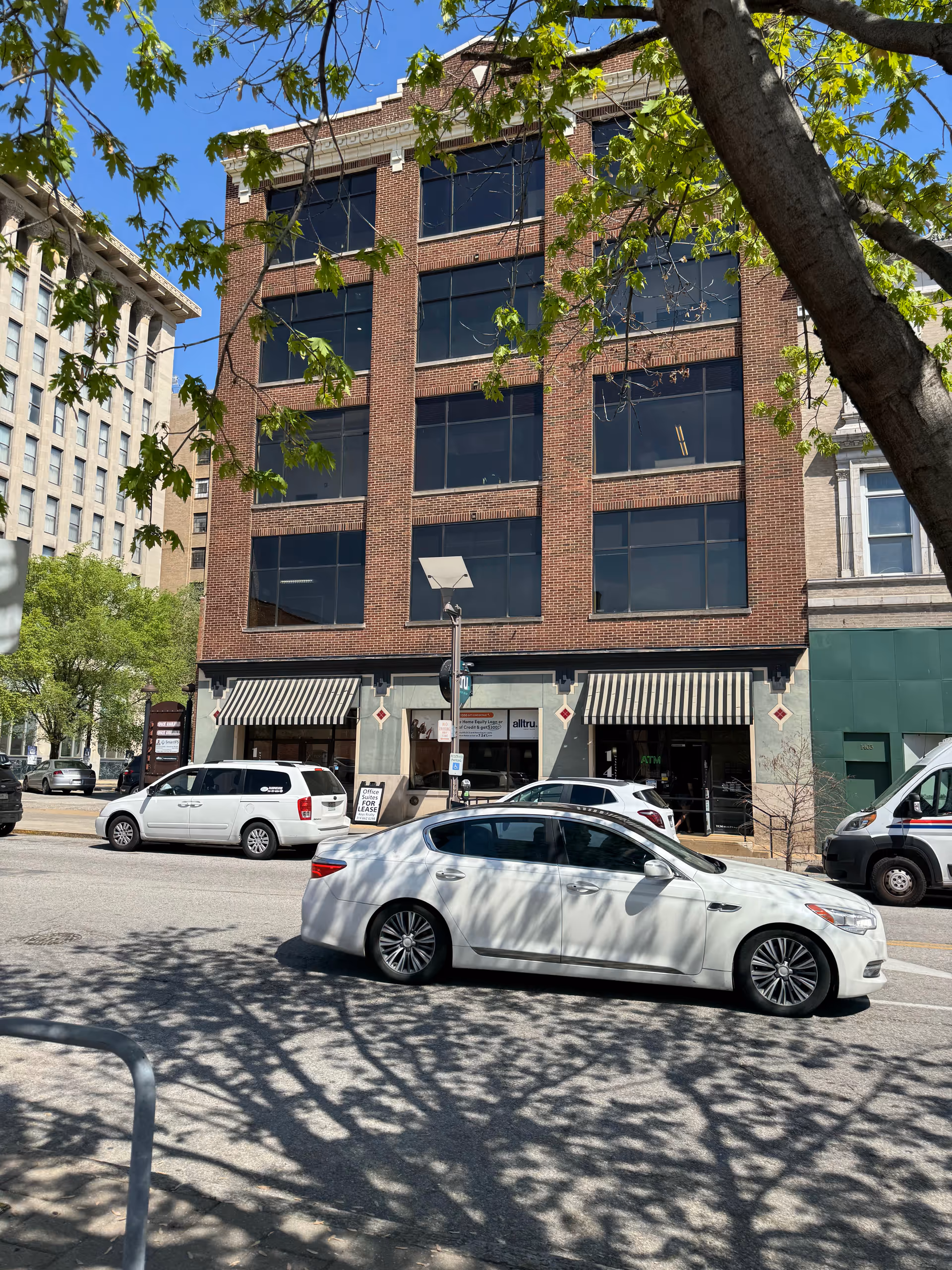 A brick, four-story building with striped awnings and parked cars on a city street.