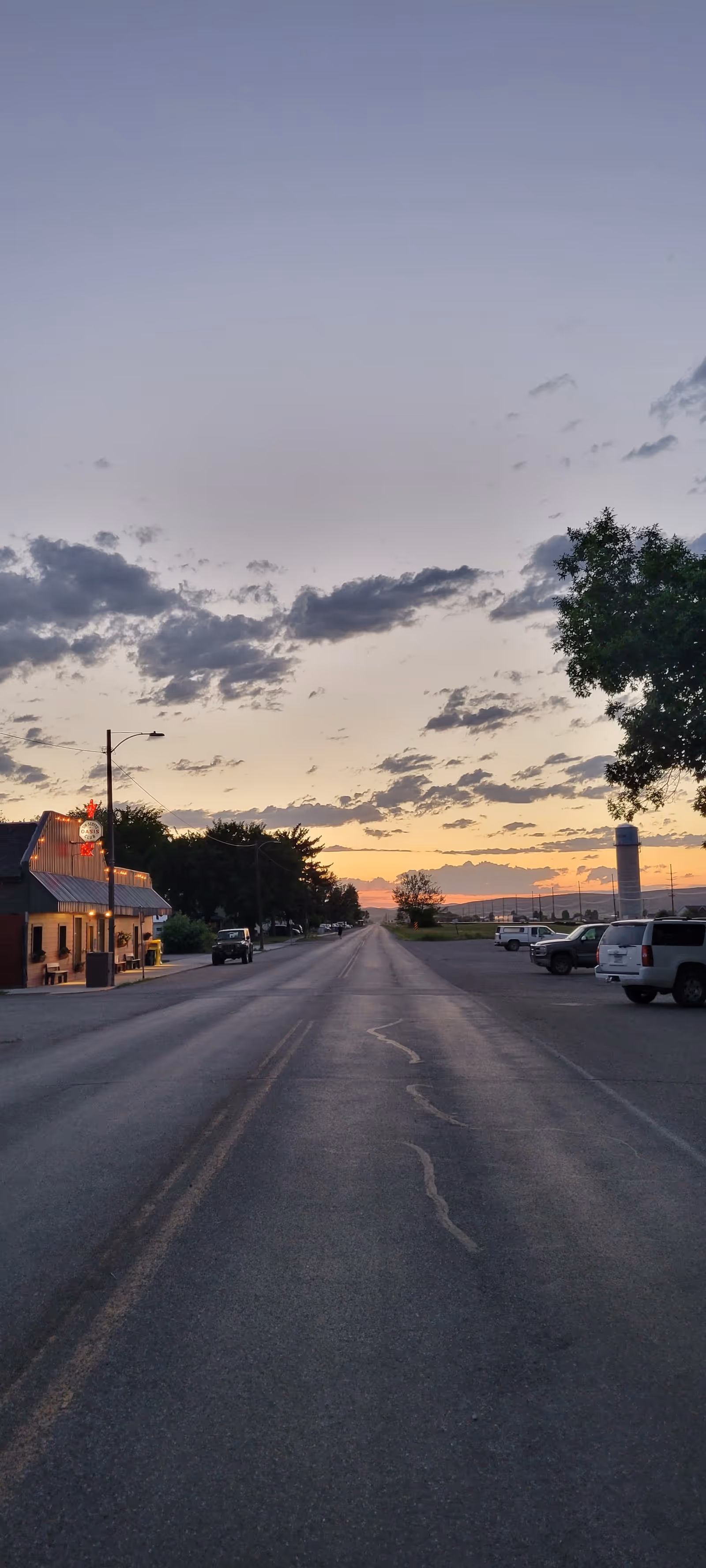 Dusk street view with a small town storefront on the left and parked cars.