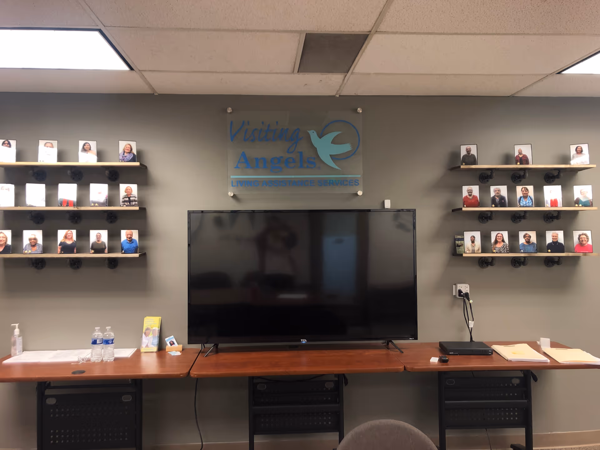 Interior lobby area with TV, signage reading Visiting Angels, and photo displays.