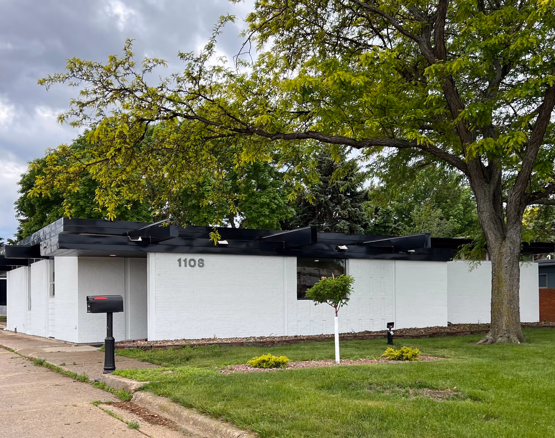 White brick building exterior with a lawn, trees, and a black mailbox.