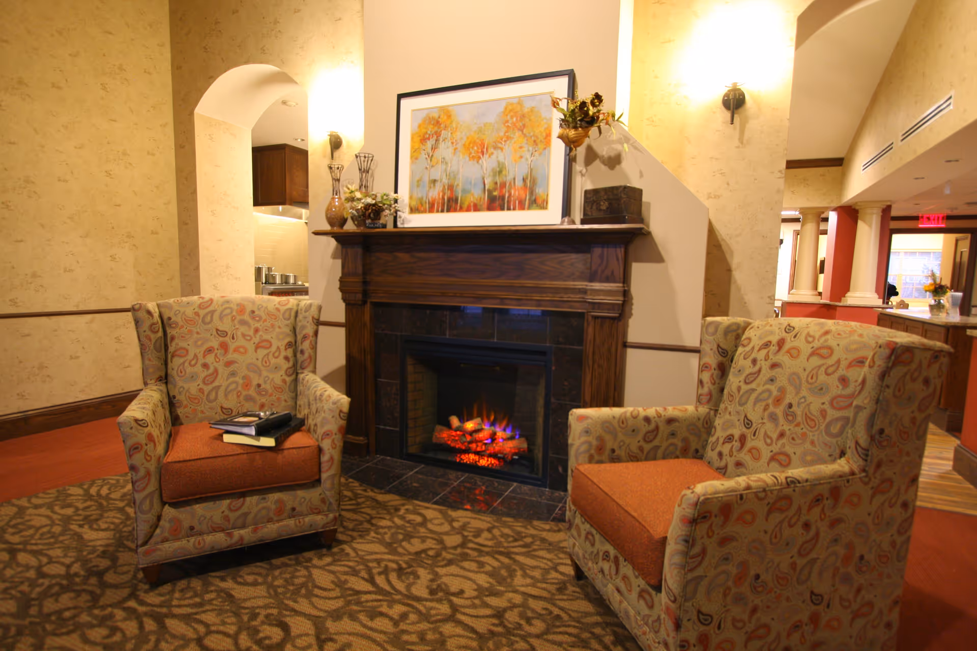Cozy lobby seating area with a fireplace, framed art, and patterned chairs.
