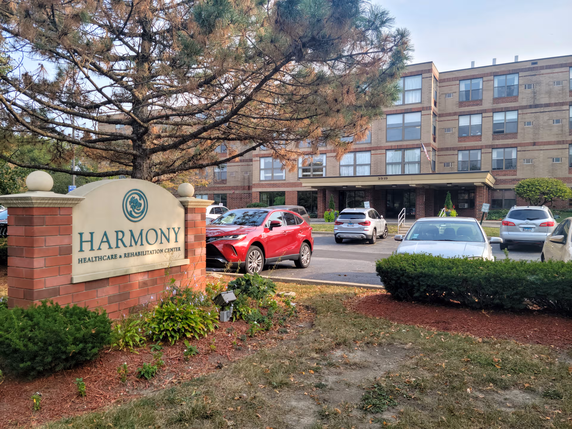 Front view of Harmony Healthcare & Rehabilitation Center showing the sign and parked cars.