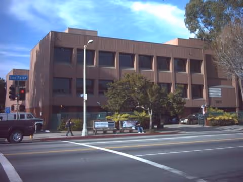 Exterior view of a multi-story brick building along a busy street with trees and pedestrians.