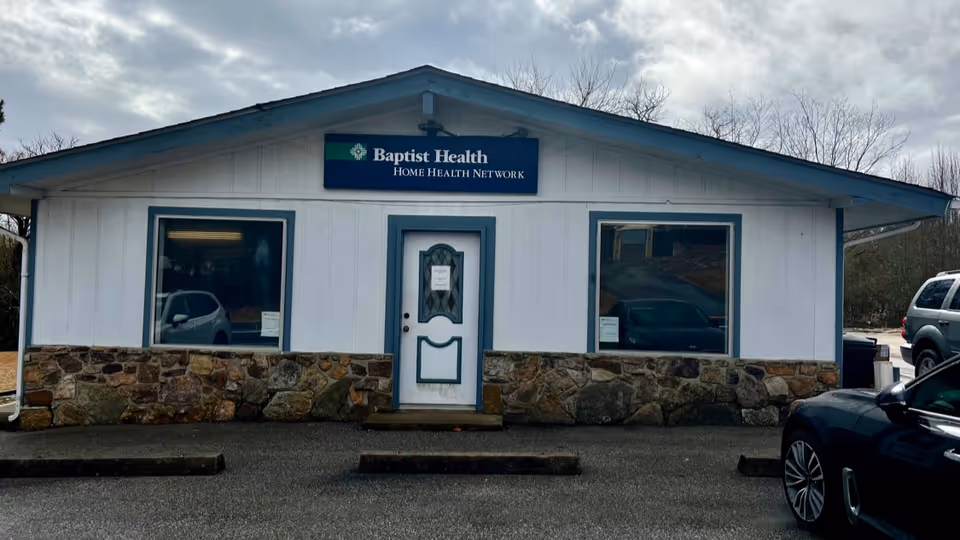 White single-story building with stone base and blue trim, Baptist Health Home Health Network sign.
