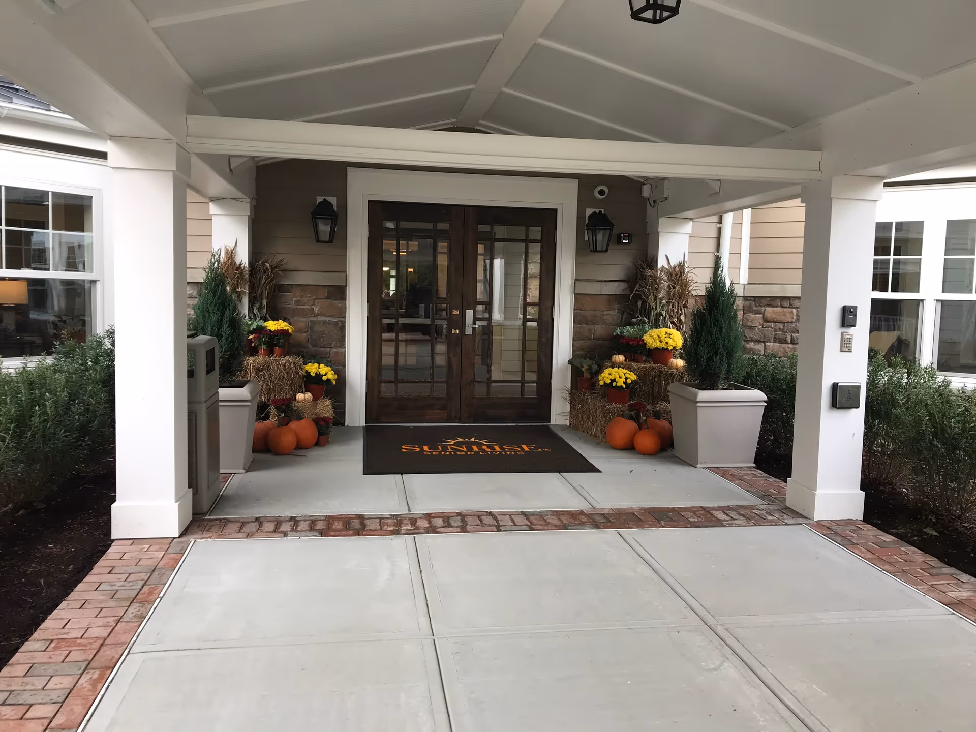 Entrance of Sunrise of Fairfield with double doors, pumpkins, and fall decorations under a sheltered porch.