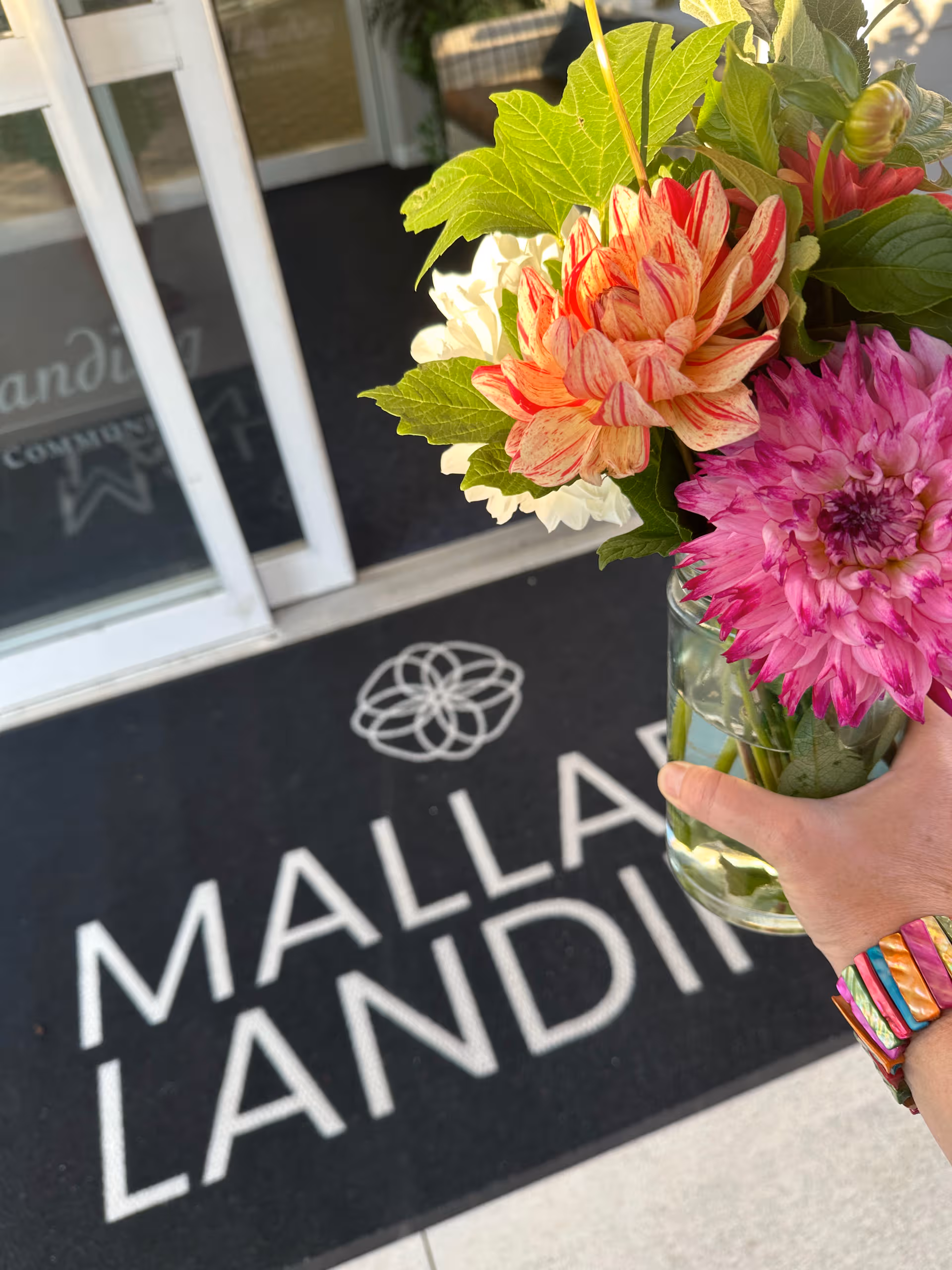 Hand holds colorful bouquet near entrance mat reading Mallard Landing at building front.