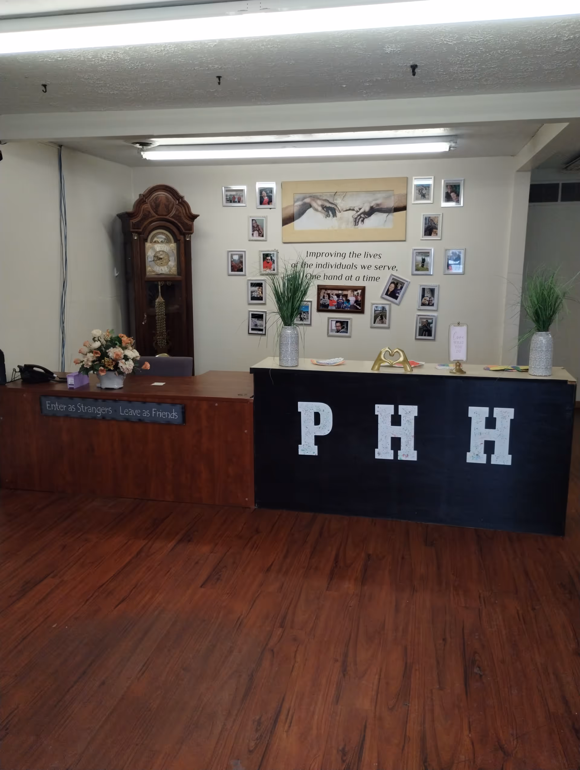 Reception desk in a lobby with PHH letters, wall photo collage, grandfather clock, and plants.