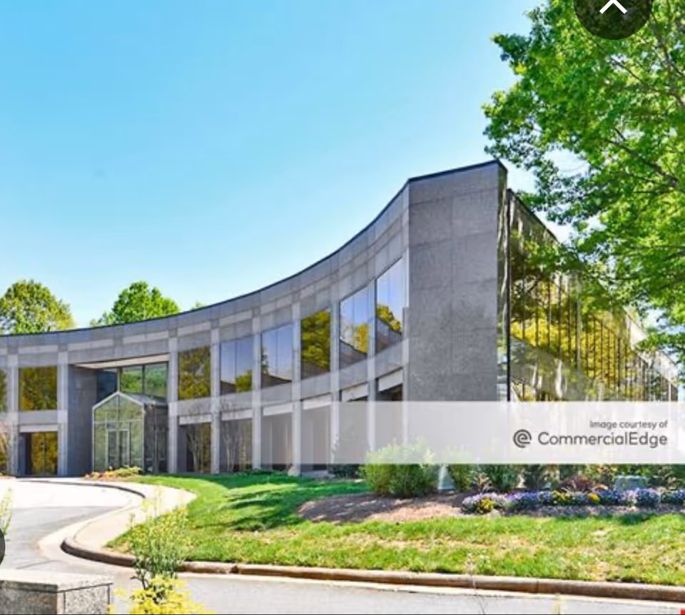 Curved glass-front facility exterior with landscaping and blue sky.
