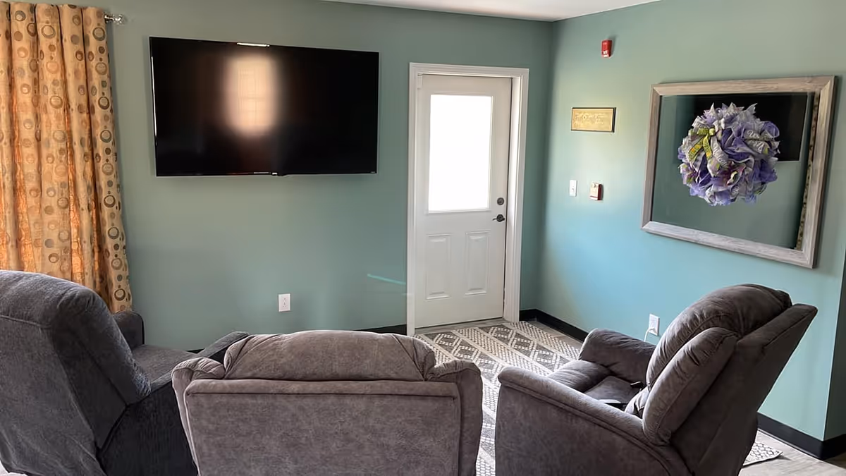 Cozy living room in a senior facility with recliners, TV, and teal walls.