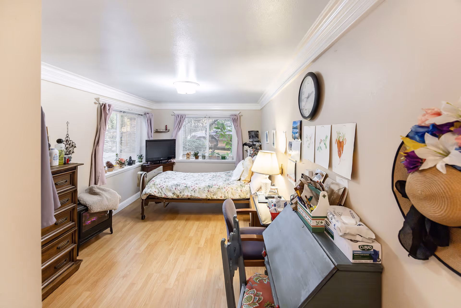 Cozy resident bedroom with bed, desk, dresser, and sunlit windows.