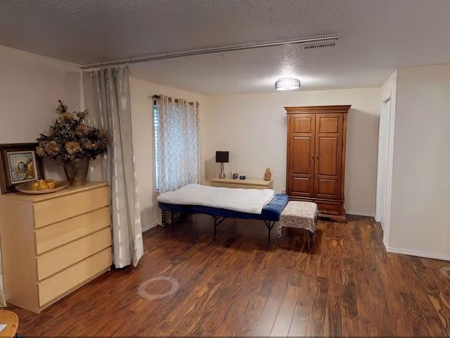 A simple bedroom featuring a bed, dresser, and decorative plants.