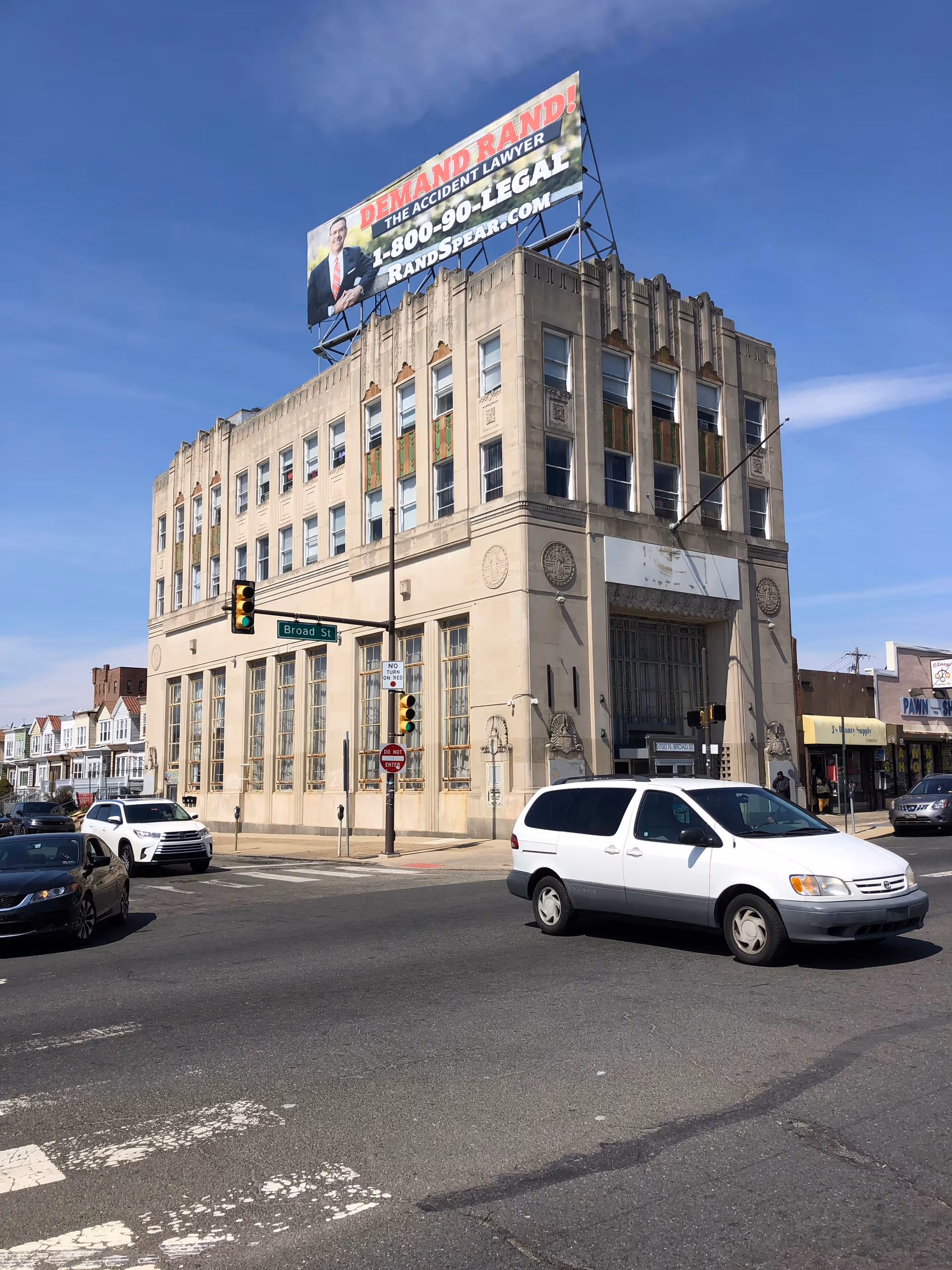 Corner street scene with a tall beige building, large billboard atop, and passing vehicles