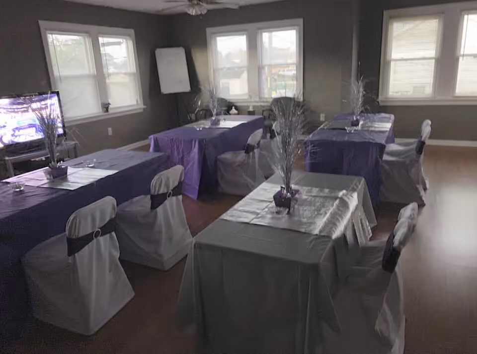 Dining room setup with purple and gray tablecloths, covered chairs, and tall centerpieces.