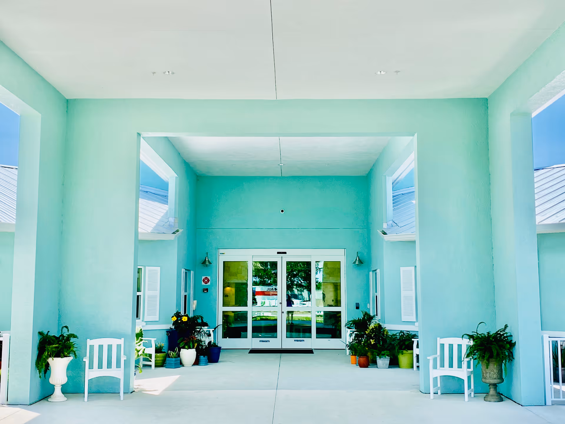 Exterior view of Trinity Place Assisted Living entrance with teal walls and potted plants.